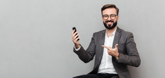 Smiling man pointing to his mobile phone.